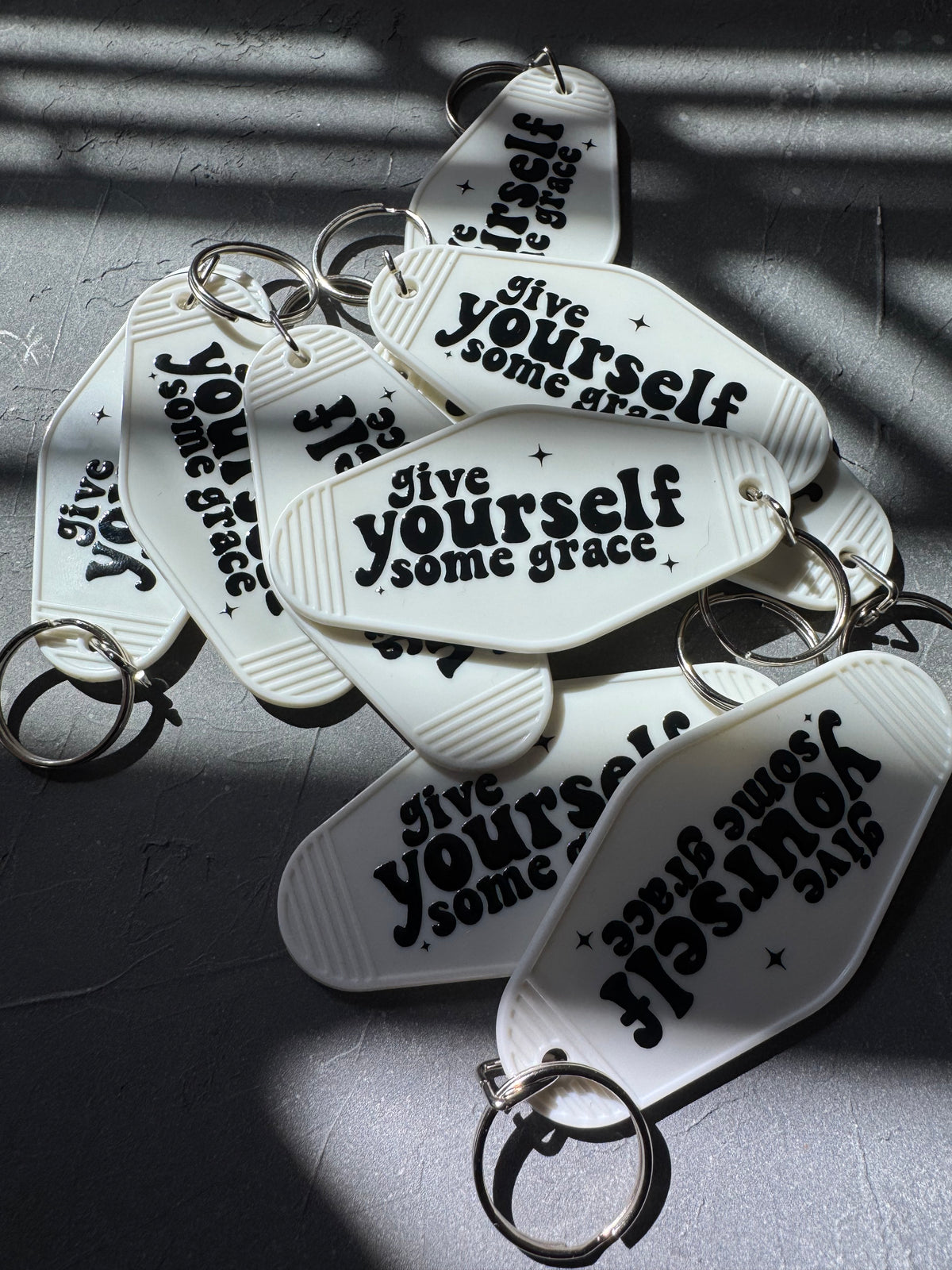 pile of white motel keychains with the words give yourself some grace on them