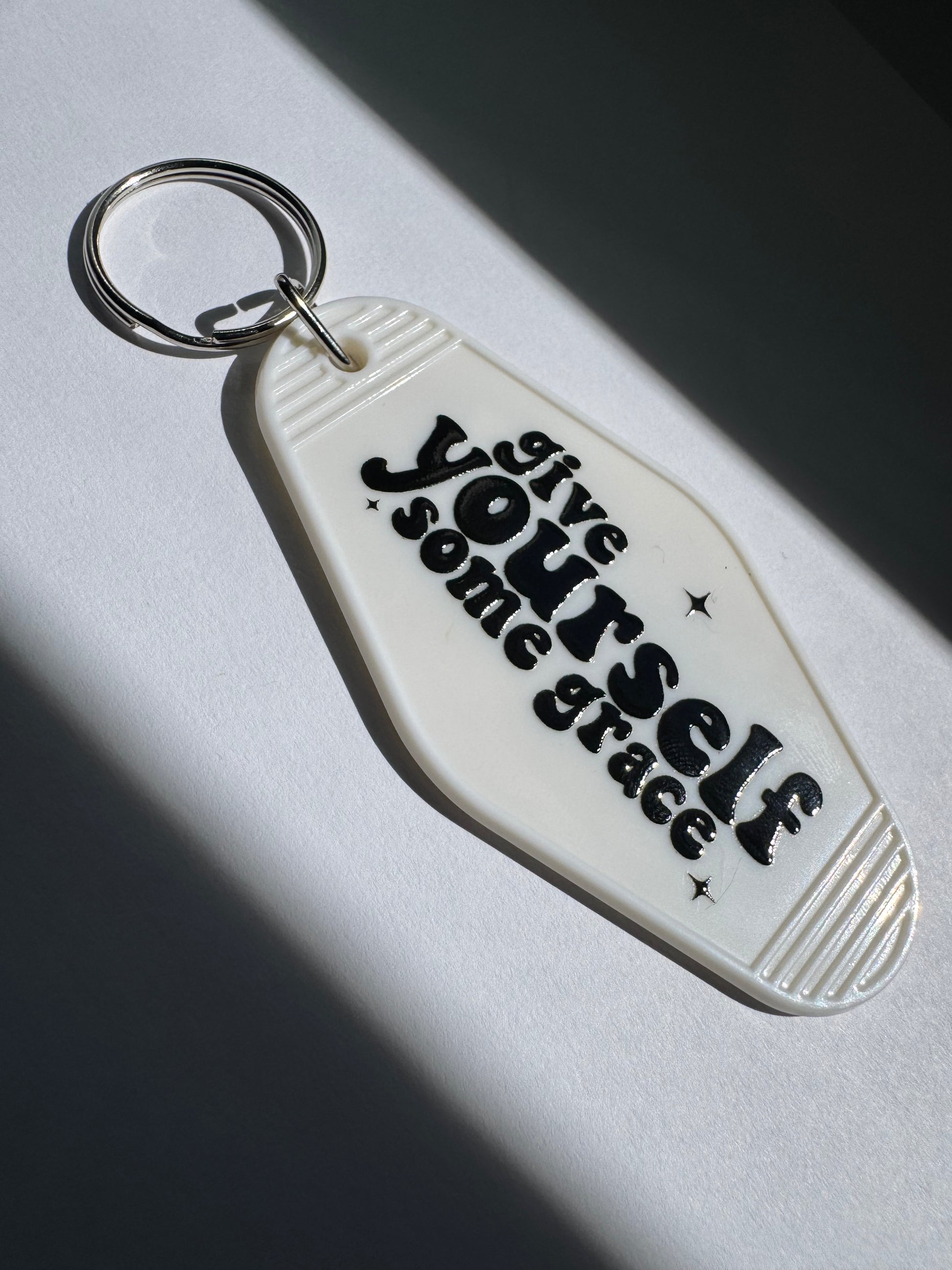 white motel keychain with give yourself some grace written in black
