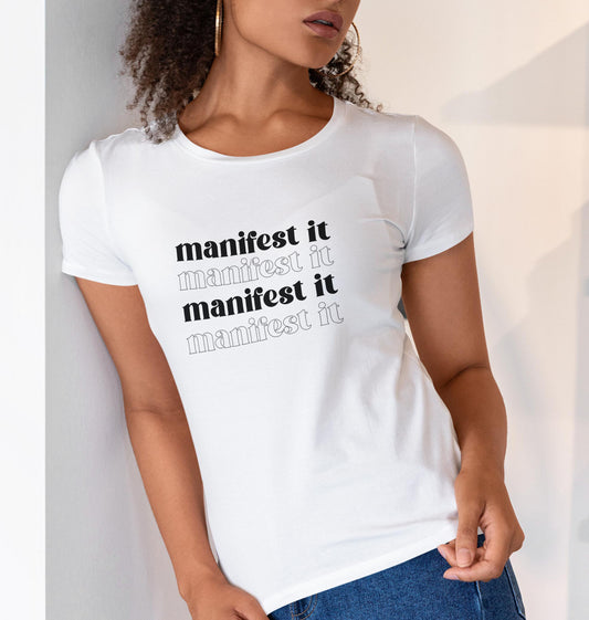 Woman in a white shirt with black writing on it that says "manifest it"